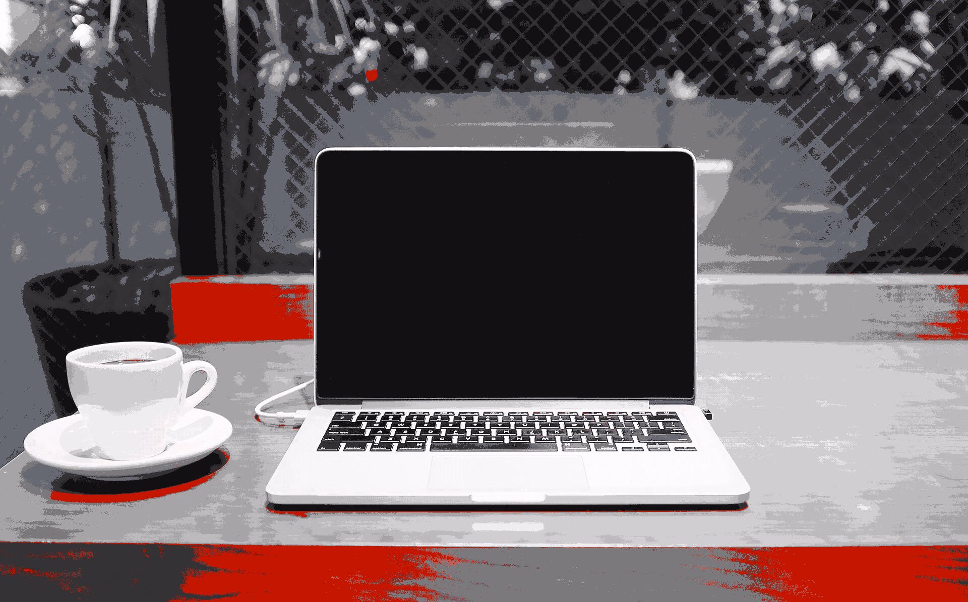 MacBook beside a white cup of coffee on a wooden cafe table